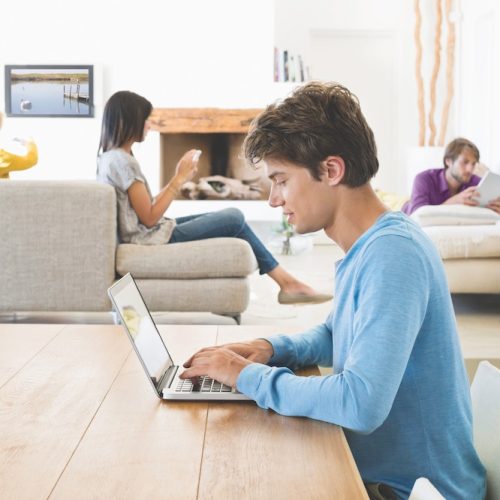 Man using a laptop with his friends using electronic gadgets in background